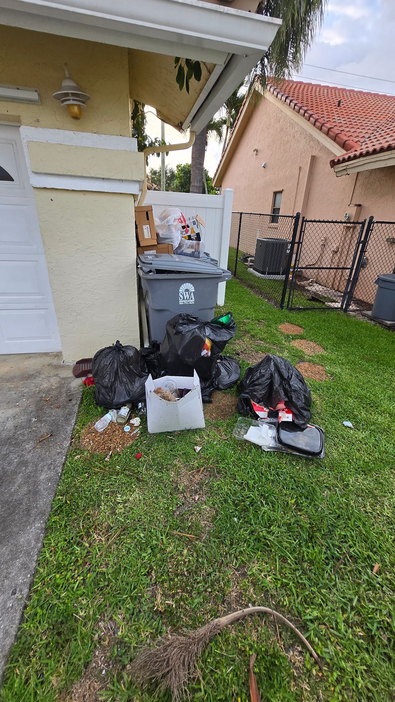 Black garbage and recycling bins beside a house with trash bags scattered on the lawn