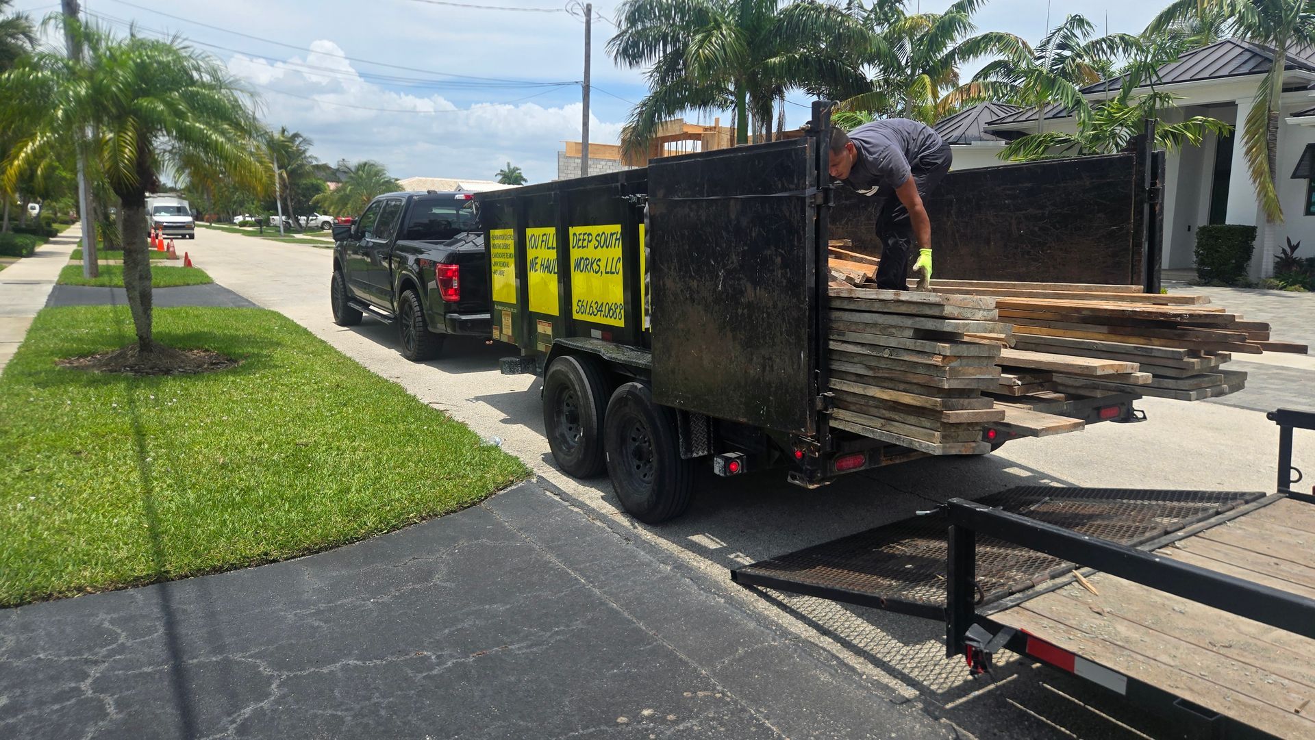 Worker loading wooden planks onto a trailer parked beside a suburban street