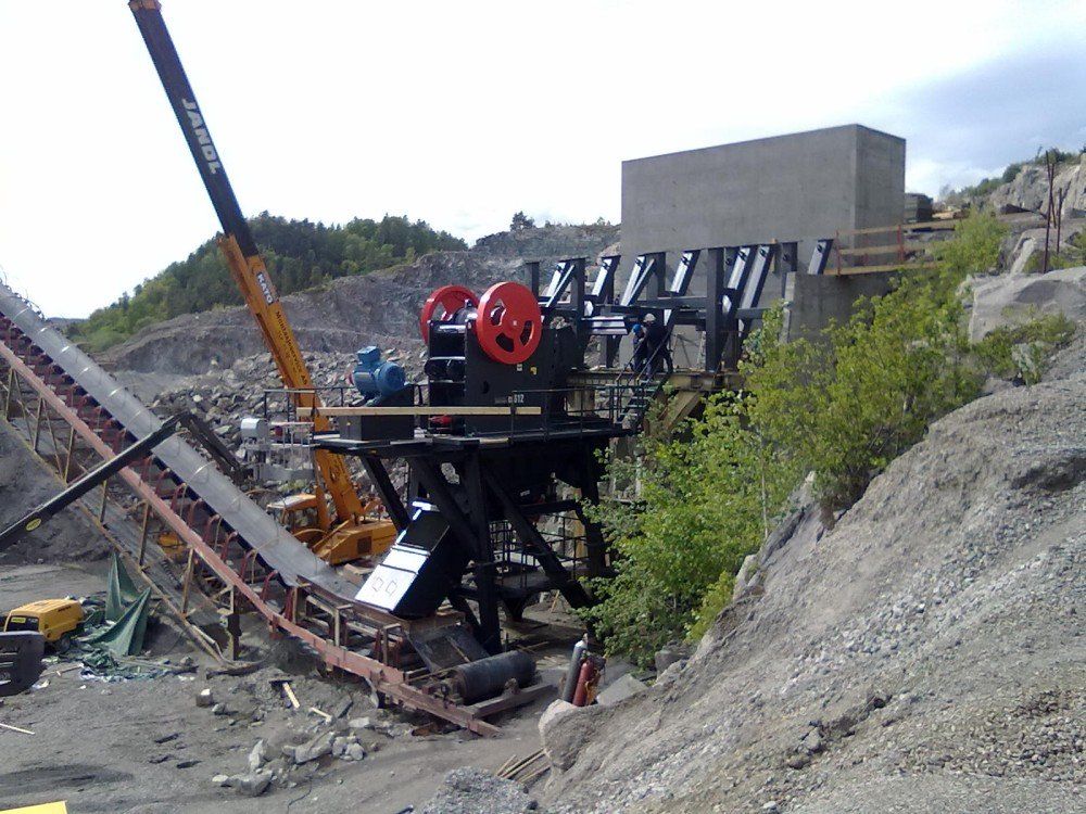 En steinknuser og et transportbånd i et steinbrudd. Kranen støtter maskinen.