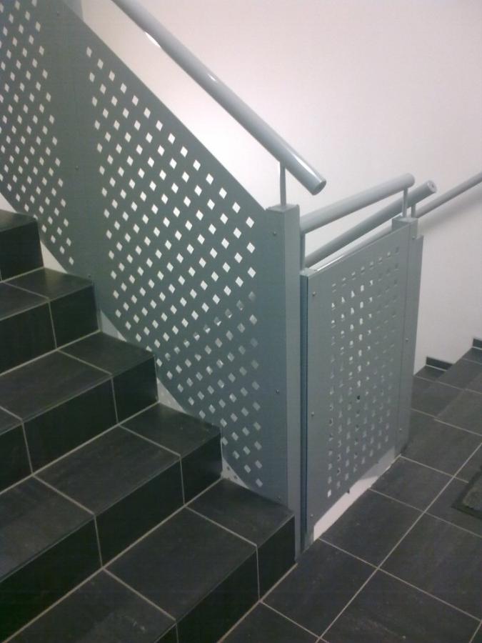 Trapp med grått perforert metallrekkverk. Svarte flislagte trinn, grå rekkverk og hvite vegger.