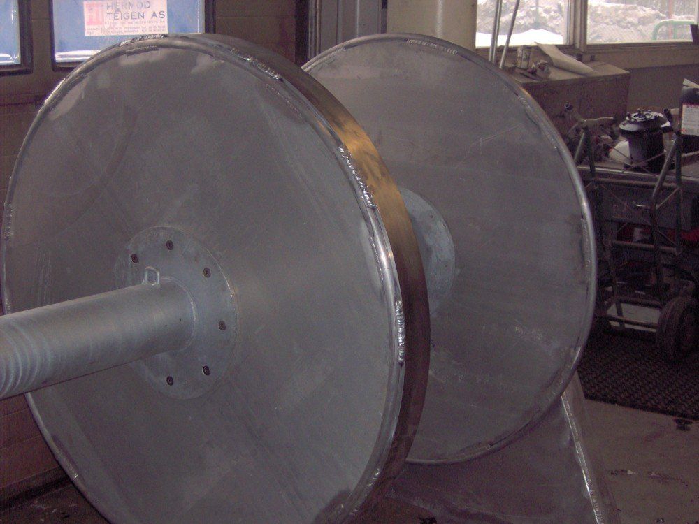 To store metallsneller på en sjakt i et verksted, muligens for vikling eller oppbevaring av kabler.