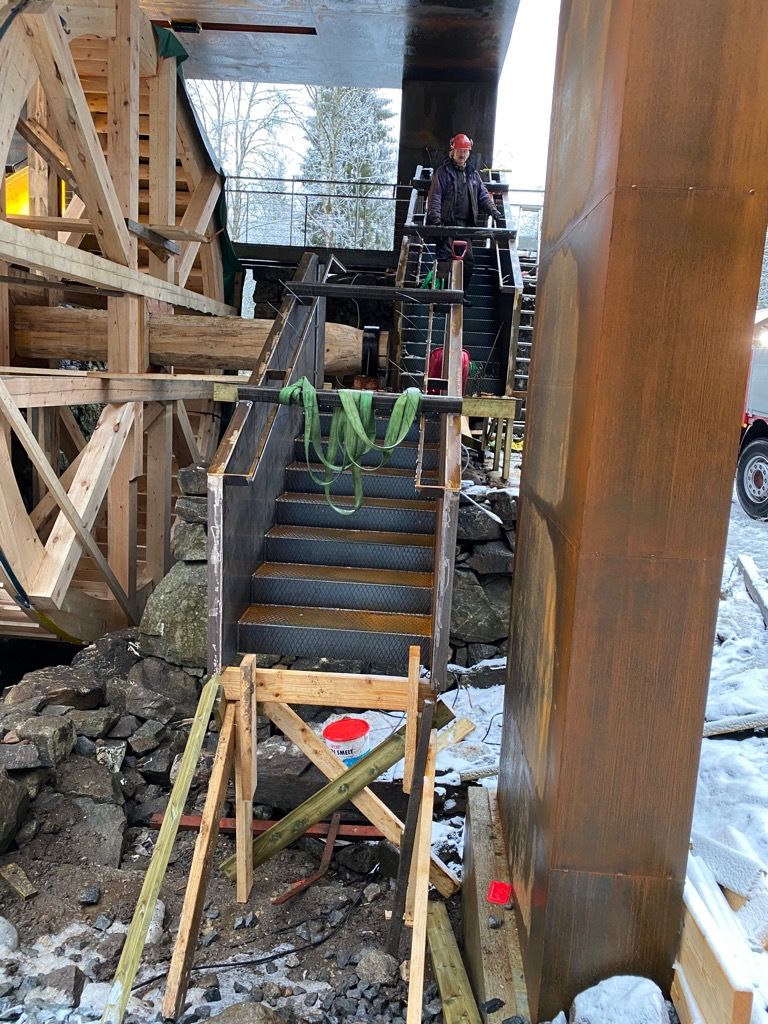 Tretrapper som fører til en plattform for vannhjul. En person står på plattformen. Snø på bakken.