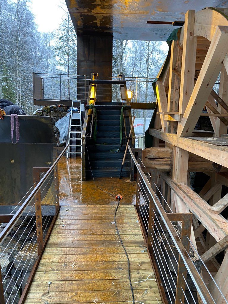 En gangvei i tre med metallrekkverk fører til trapper og struktur; omgivelsene er utendørs.