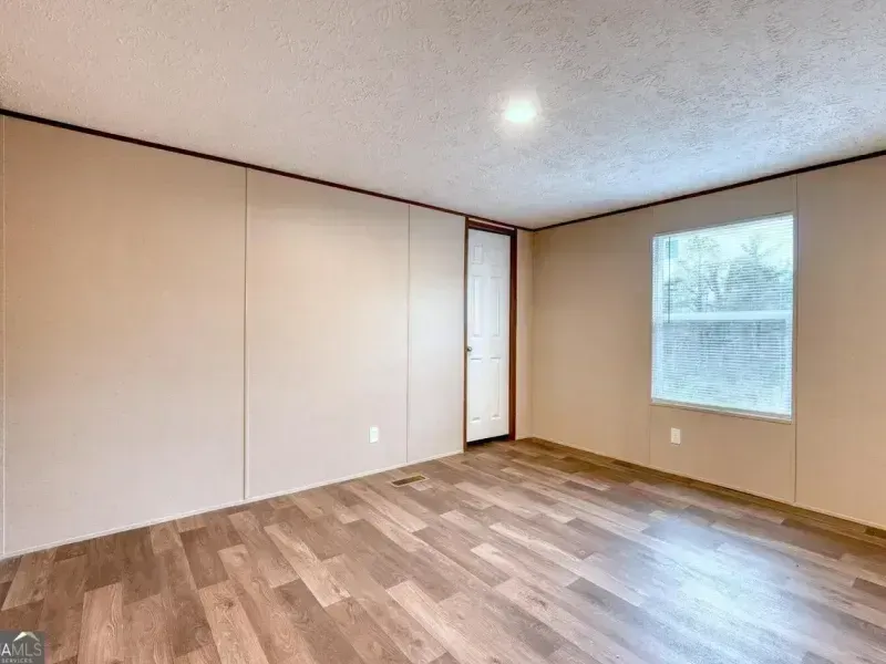 Empty beige room with wood flooring and a window letting in daylight