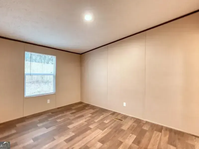 Empty beige room with wood floor, a small window, and a ceiling light.