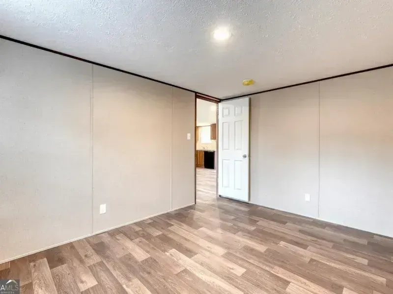 Empty room with gray walls, wood floors, and a white door near the back.