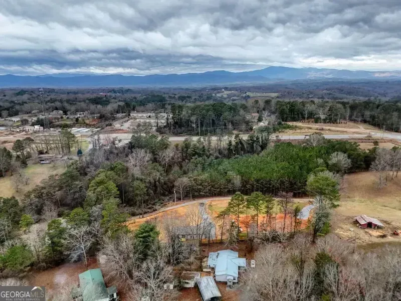 Aerial view of a rural landscape with trees, scattered buildings, and mountains under a cloudy sky