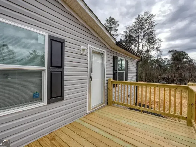 House exterior with a wooden deck, white siding, and a railing overlooking trees