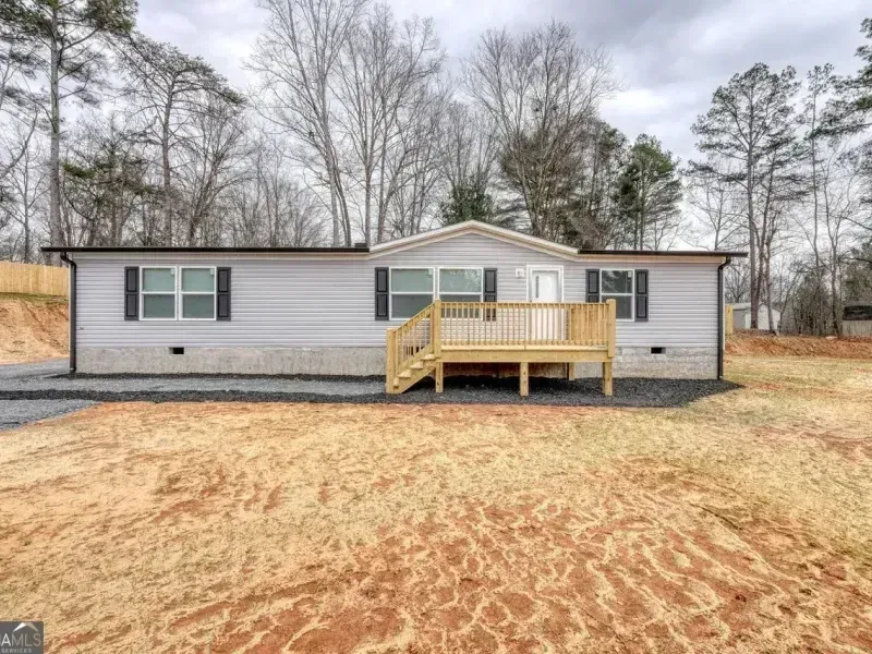 Single-story white house with a small wooden front deck in a bare yard under cloudy skies