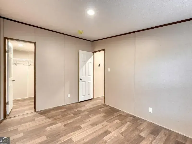 Empty beige bedroom with wood-look flooring and open closet and doorway.