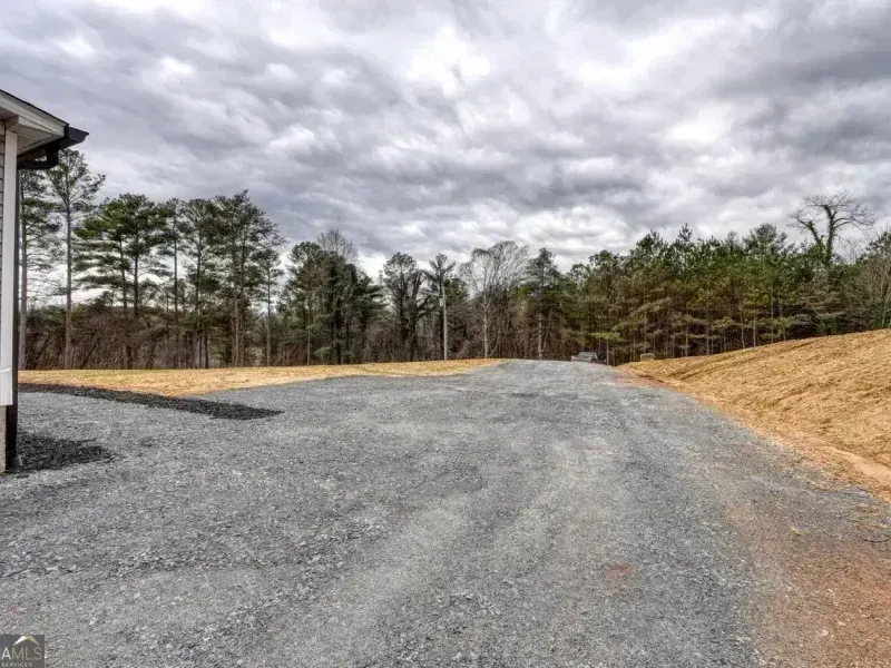 Gravel driveway leading past a wooded lot under a cloudy sky