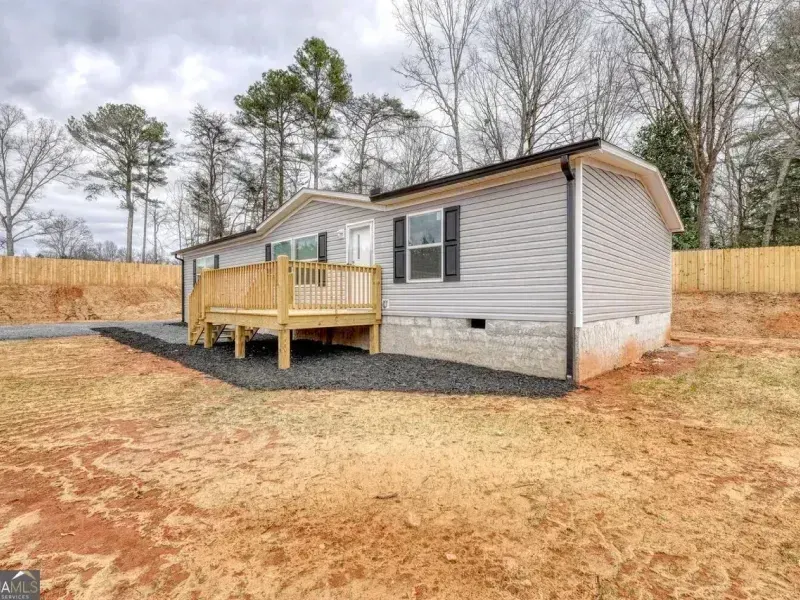 Single-story gray house with a small wooden porch on a cleared lot surrounded by trees.