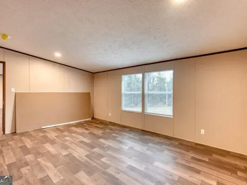 Empty beige living room with wood-look flooring, two windows, and sliding closet doors