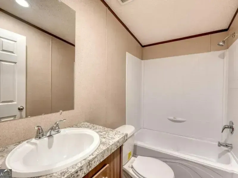 Small beige bathroom with vanity, sink, mirror, and a shower/tub combo with white curtain and walls