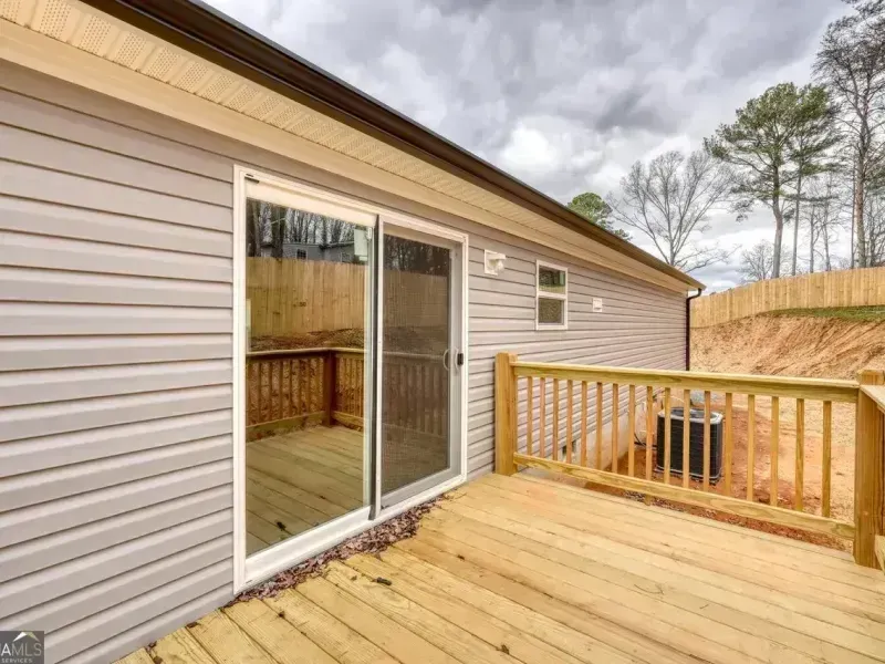 Wooden deck with sliding glass door and railing beside a beige house under cloudy skies