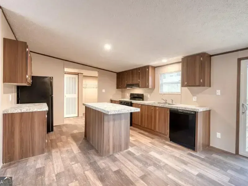 Empty modern kitchen with wood cabinets, island, black appliances, and light gray flooring
