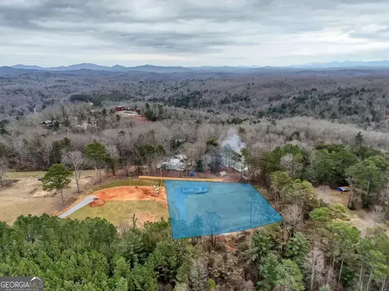 Aerial view of a wooded construction site with orange and blue tarps beside a cleared hillside.