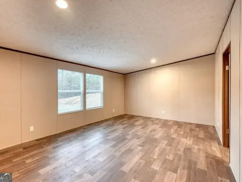 Empty beige room with wood-look floor, window, and recessed ceiling lights
