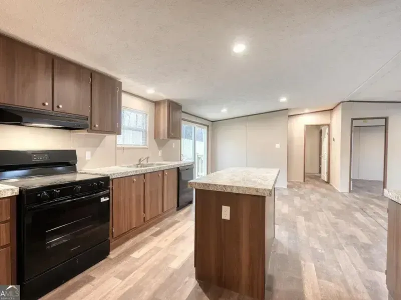 Modern kitchen with dark cabinets, black appliances, white countertops, and an island in an open room