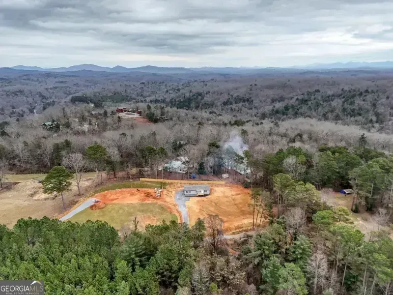 Aerial view of a red clay baseball field surrounded by trees and rolling hills under a cloudy sky