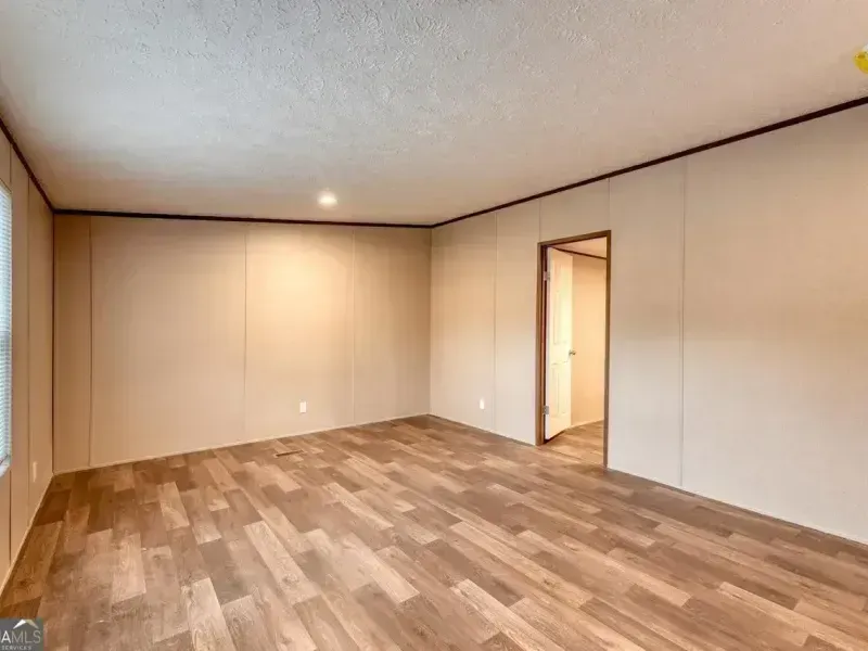 Empty beige room with wood-look flooring, white ceiling, and an open doorway