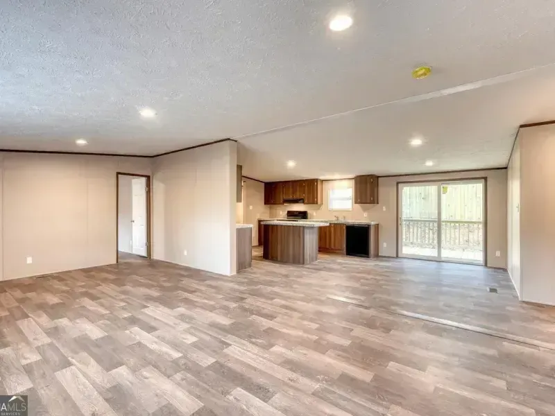 Empty open-plan living room with wood-look floors, kitchen, and sliding glass doors.