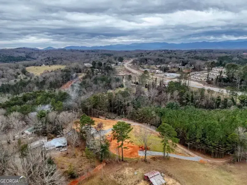 Wide rural landscape with winding road, scattered trees, and cloudy sky over distant hills