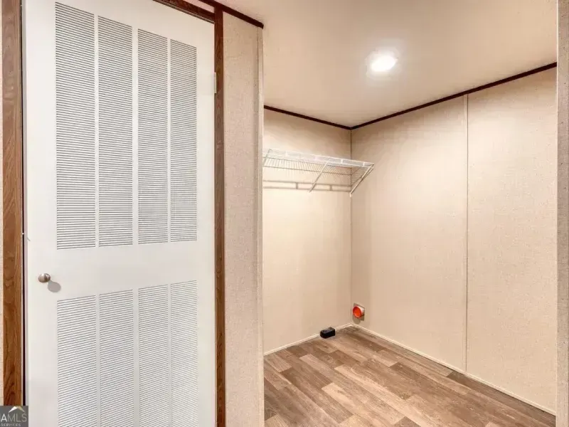 Empty walk-in closet with beige walls, wood-look floor, wire shelves, and an open white louvered door.