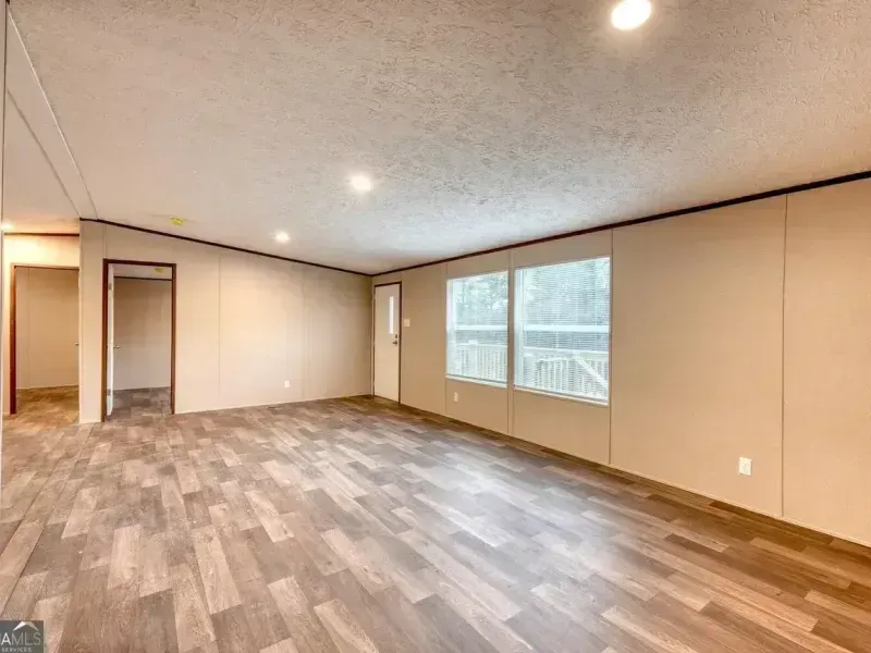 Empty beige living room with wood-look flooring, recessed lights, and a large window.