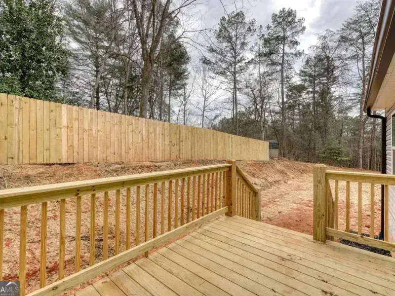 Wooden deck overlooking a fenced backyard with trees and a dirt slope