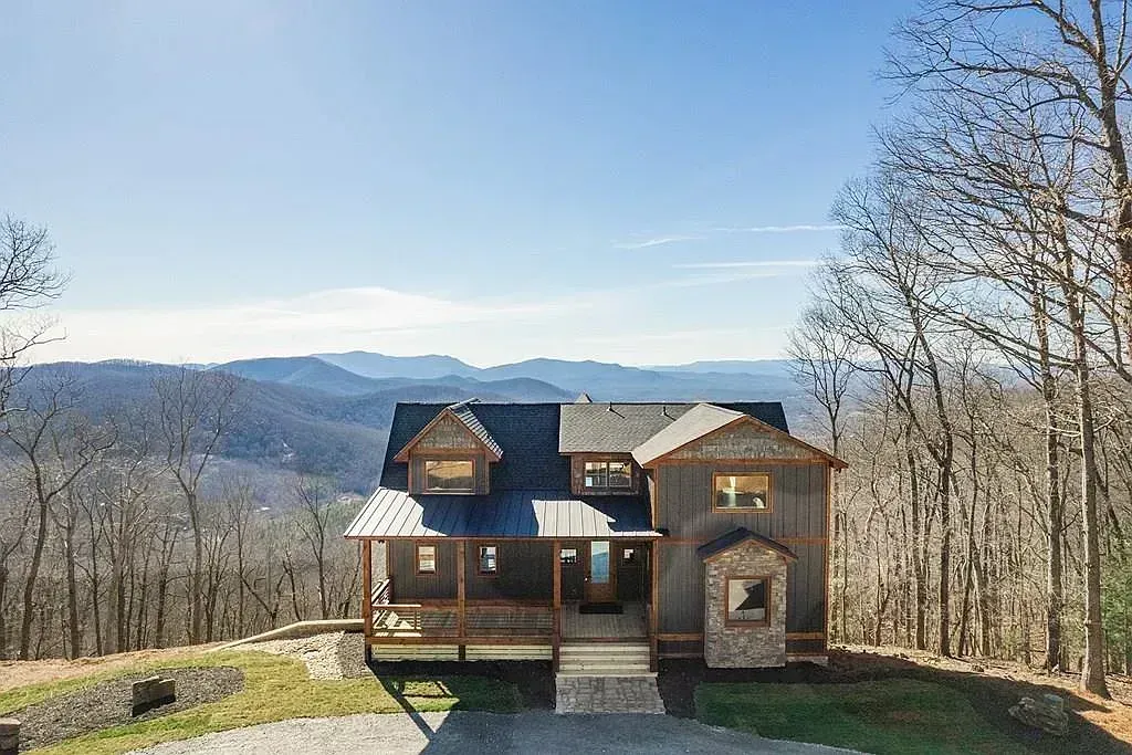 Wooden cabin on a hill with a mountain view, leafless trees, and a clear blue sky
