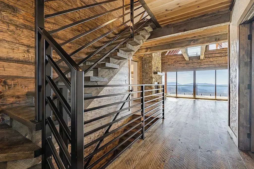 Rustic attic stairwell with wooden beams, metal railing, and large windows overlooking the landscape