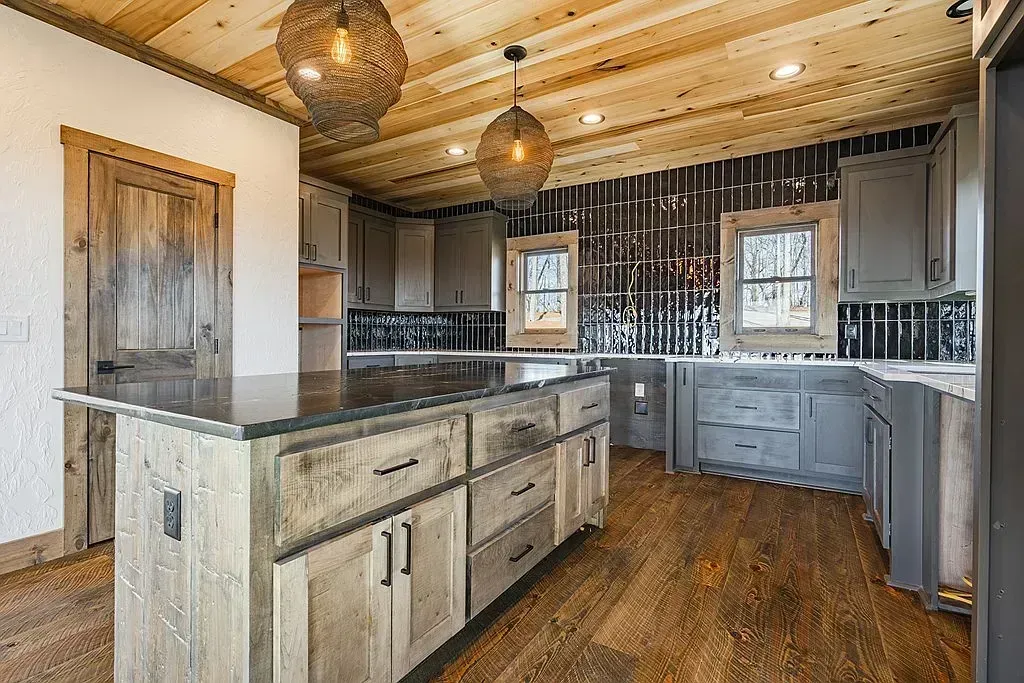 Rustic kitchen with wood cabinets, stone island, dark backsplash, and hanging pendant lights