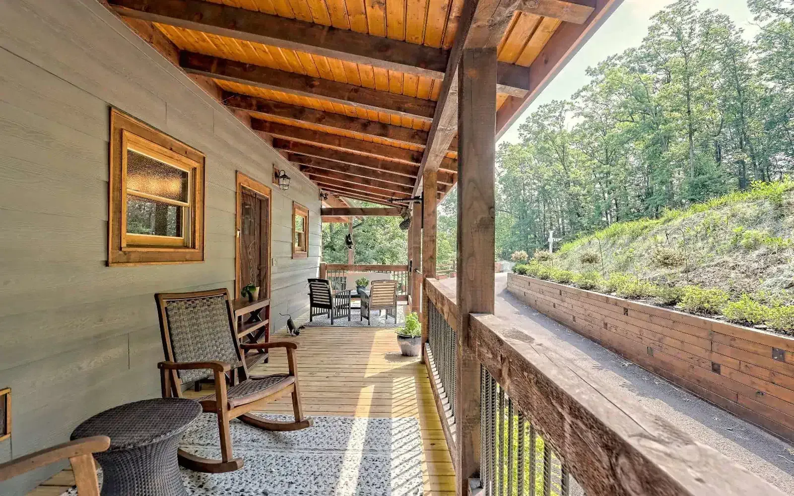 Covered wooden porch with rocking chairs, framed art, and forest view along a rustic cabin exterior