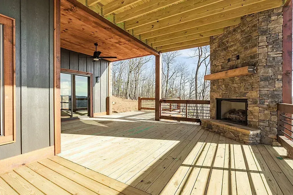 Covered wooden porch with stone fireplace, open railing, and sunlit views of bare trees