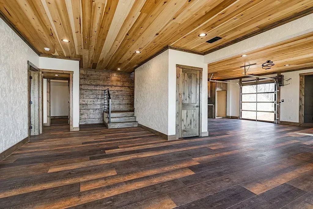 Empty rustic room with wood ceiling, dark floors, and white walls with doorways.
