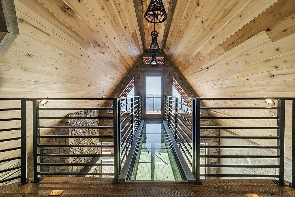 Wood-paneled loft hallway with black railings and a hanging lantern, leading to a bright doorway.