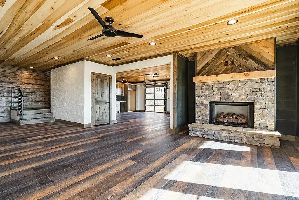 Rustic open living room with wood ceiling, stone fireplace, and dark hardwood floors