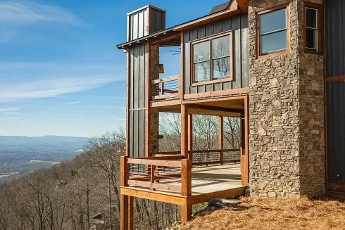 Modern cabin with large windows on a hillside overlooking a distant valley under a blue sky