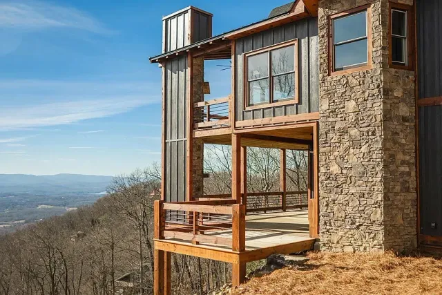 Modern cabin with large windows on a hillside overlooking a distant valley under a blue sky