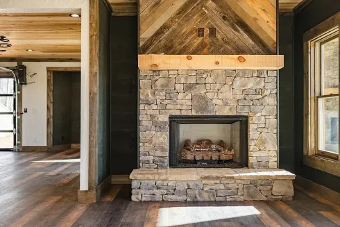 Rustic living room with stone fireplace, wood floors, and large windows.