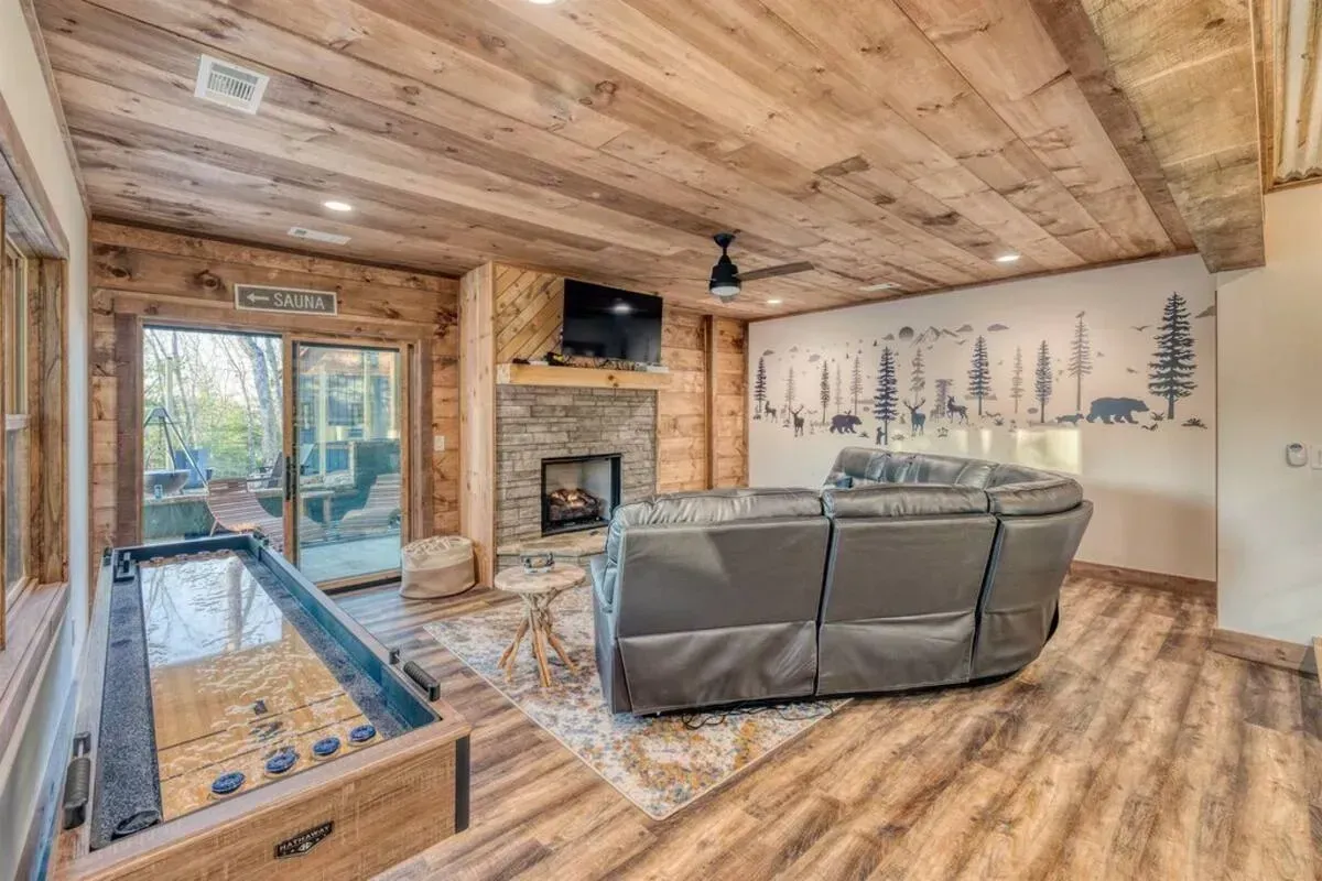 Cozy log cabin living room with fireplace, gray sofa, and large wall art overlooking a deck
