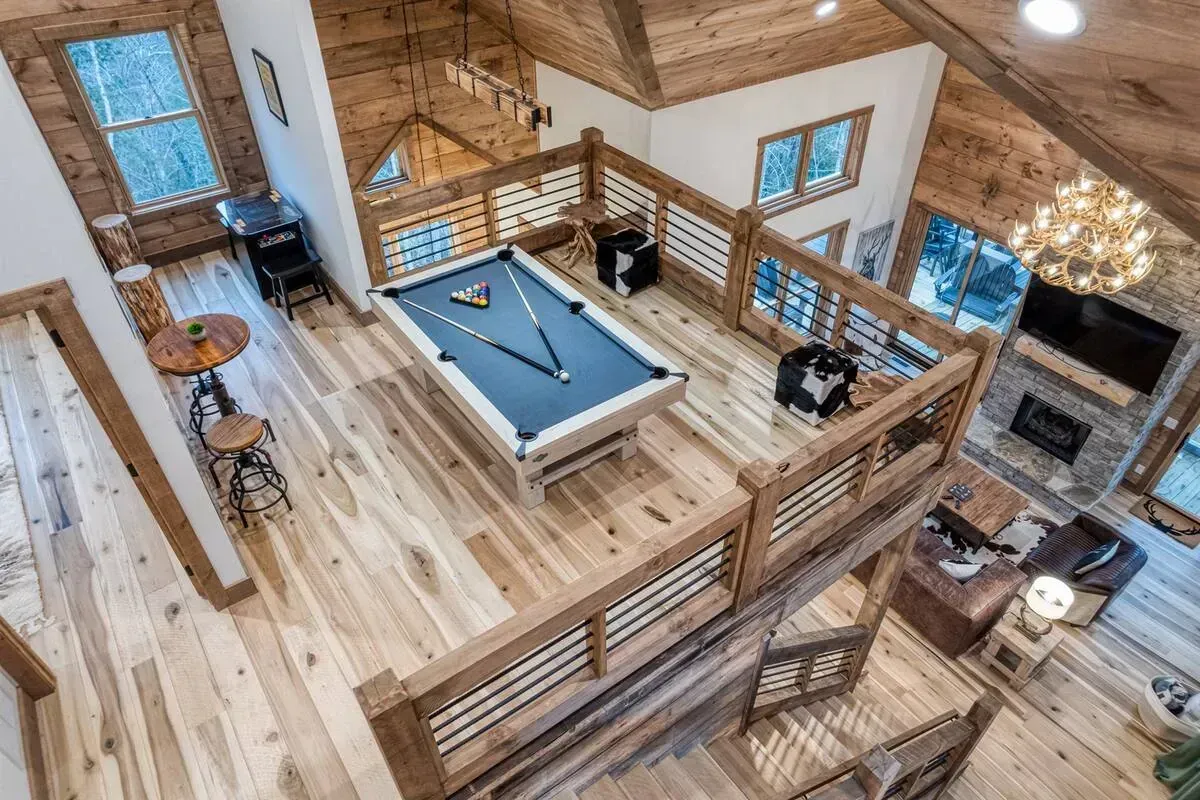 Loft game room with a pool table, wooden railings, and a brick fireplace under vaulted ceilings