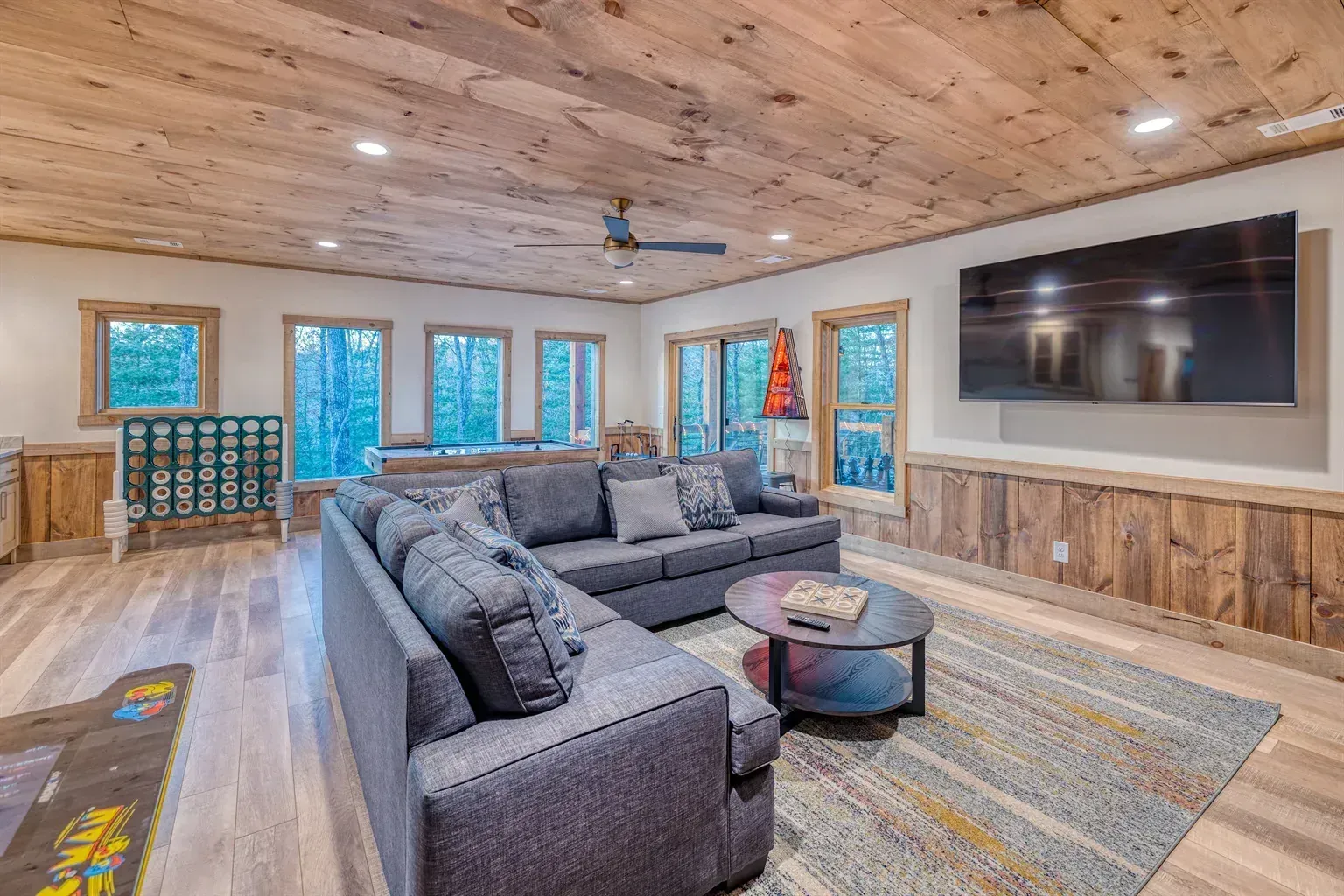 Modern living room with gray sectional, wood ceiling, large wall TV, and blue-trimmed windows