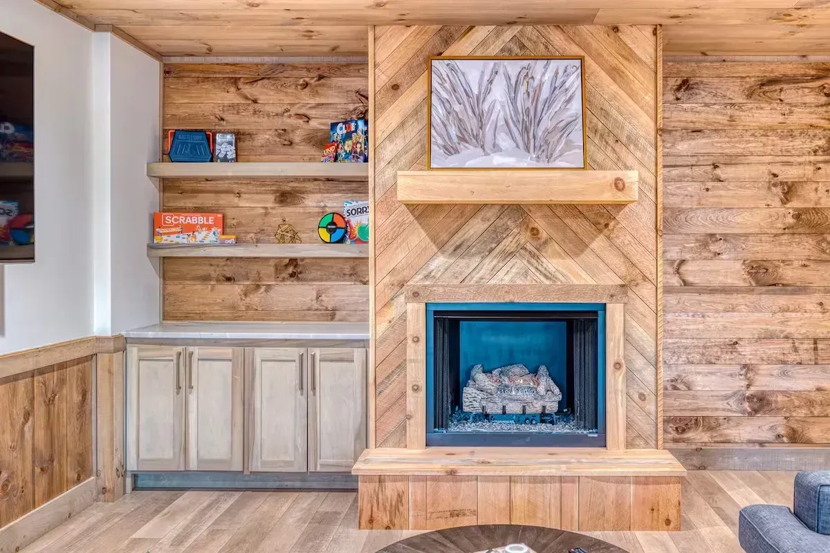 Built-in wooden entertainment wall with shelves, cabinets, and a blue-trimmed fireplace in a rustic room