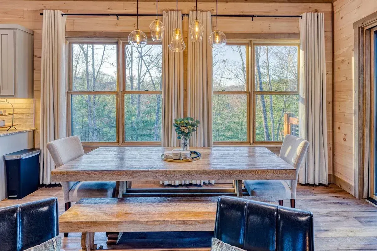 Bright dining room with large windows, rustic wood walls, and a long wooden table with benches
