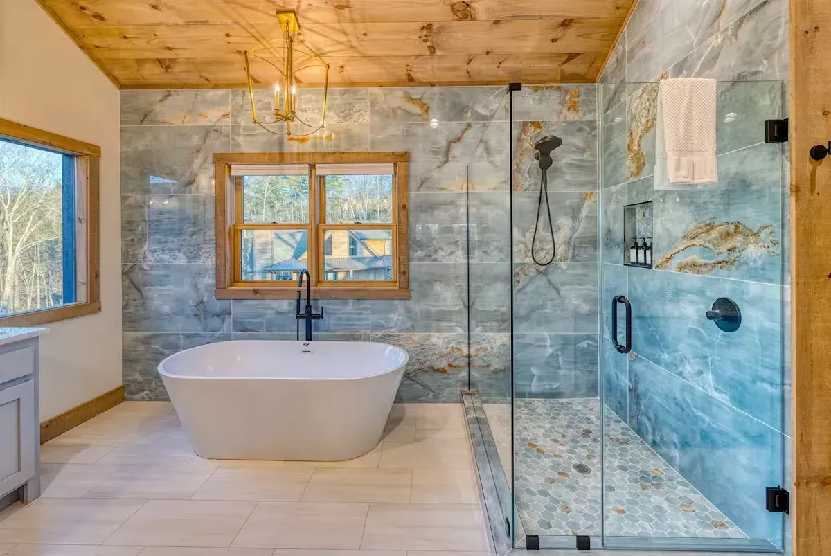 Modern bathroom with freestanding tub, glass shower, wood ceiling, and blue stone walls