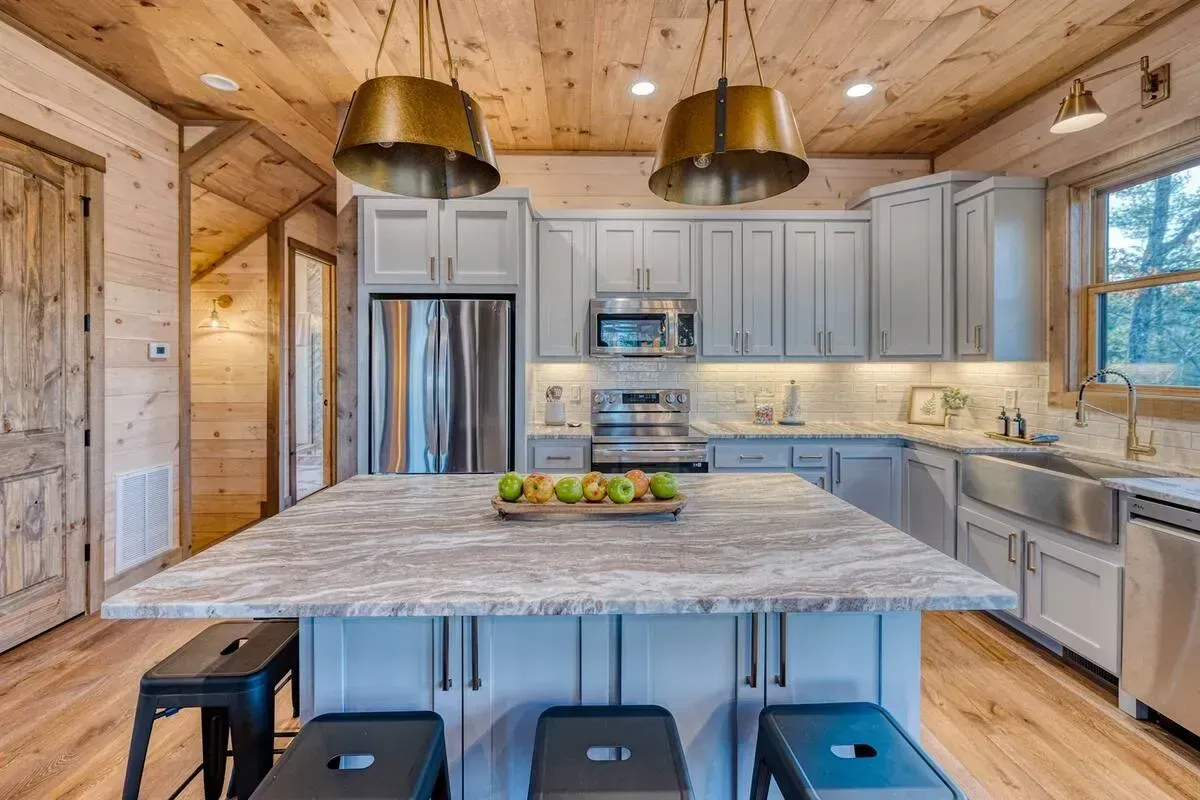Modern kitchen with marble island, stainless appliances, wood walls, and pendant lights