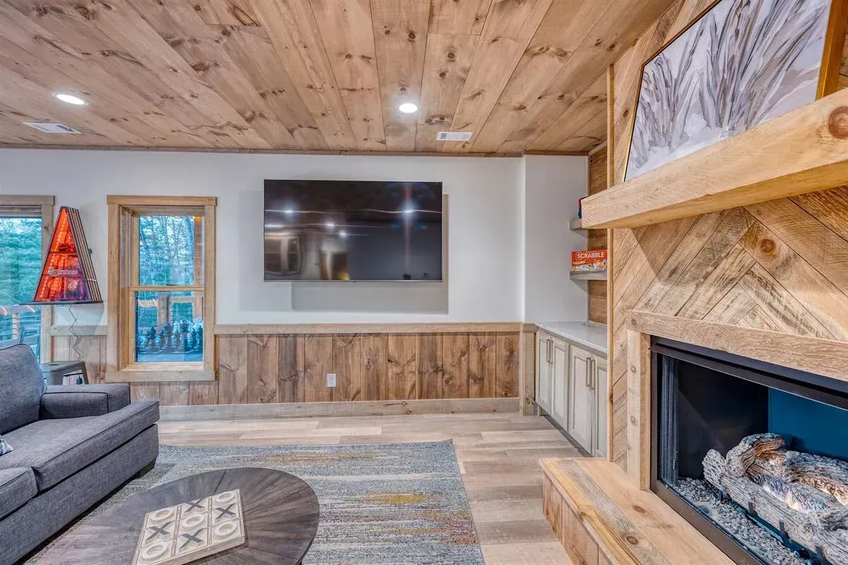 Modern living room with wood ceiling, stone fireplace, gray sofa, and wall-mounted TV