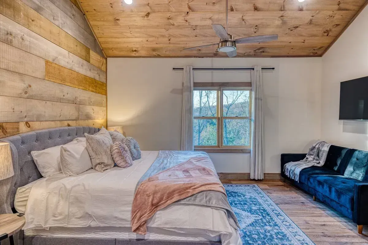 Cozy bedroom with wood ceiling, large bed, blue sofa, and window with curtains